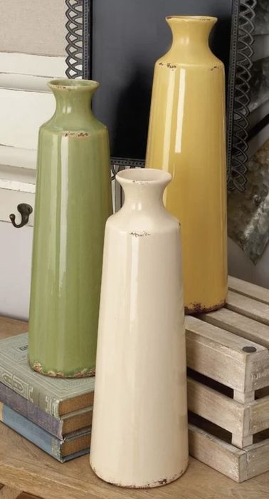 Three tall ceramic vases arranged on a wooden surface alongside books and a wooden crate