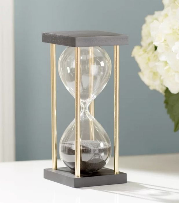 An hourglass placed on a white table with a bouquet of white flowers in the background