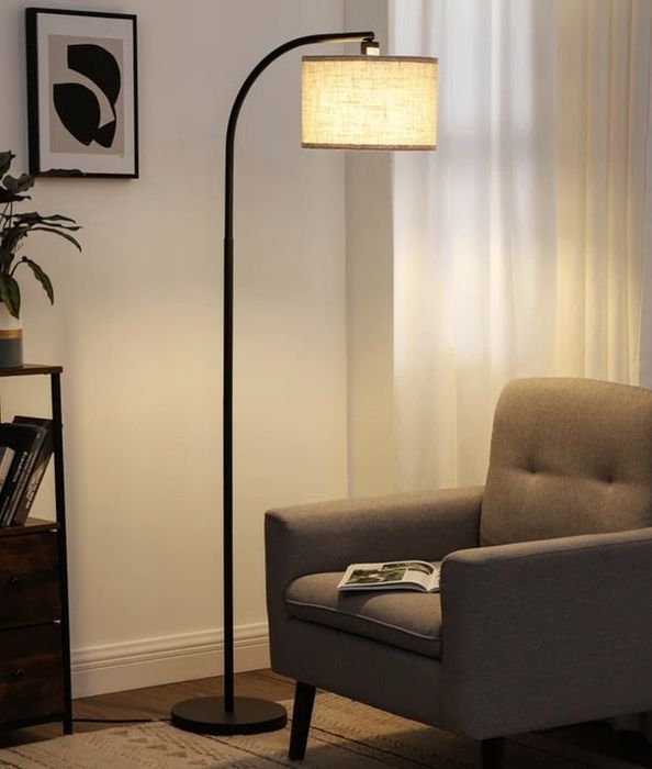 A curved floor lamp paired with a cozy armchair, placed near a window with sheer curtains