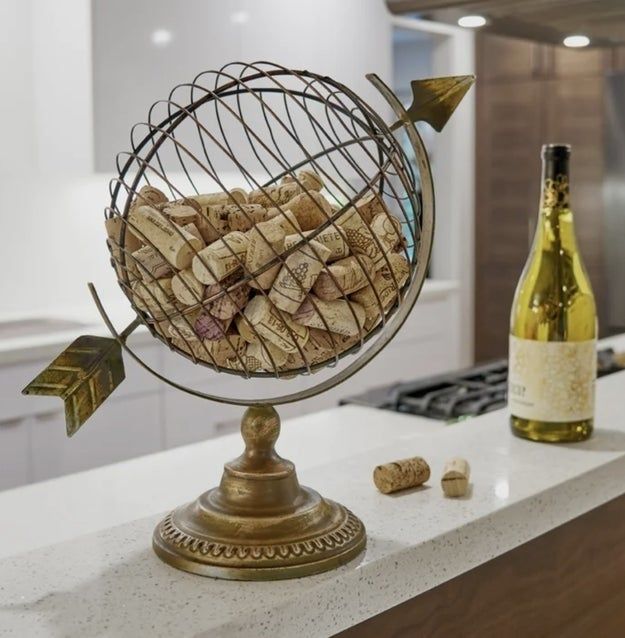 A wine cork holder shaped like a globe, filled with corks, placed on a kitchen counter beside a wine bottle