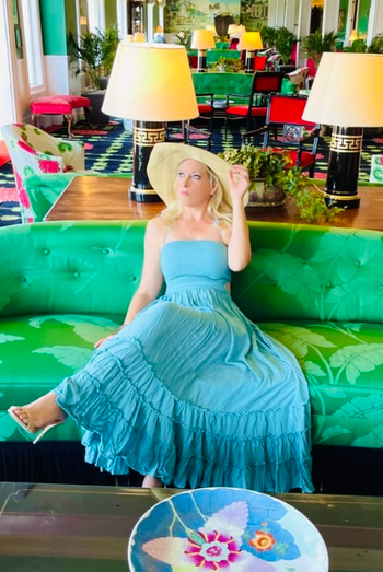 reviewer seated in a hotel lobby, wearing the dress in a striking blue shade