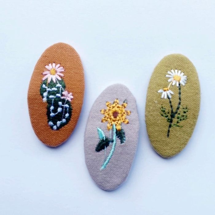 Brown, gray, and olive oval-shaped clips, each featuring a unique embroidered flower