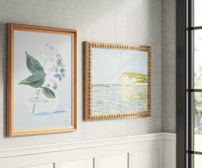 Two framed artworks displayed on a wall, one featuring floral motifs and the other showcasing a coastal scene