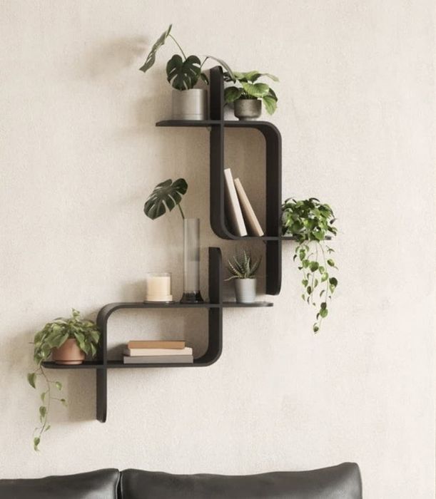 Wall-mounted shelves adorned with potted plants and small decorative pieces, positioned above a sleek black leather couch