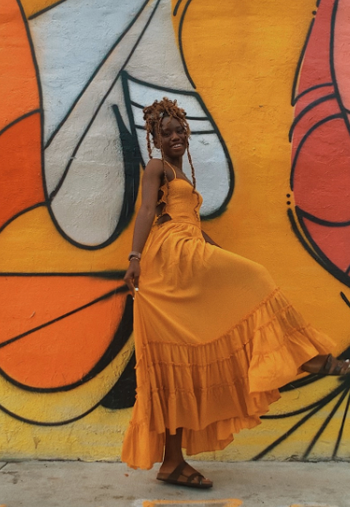 reviewer posing in front of a mural wall, wearing the dress in a vibrant orange hue