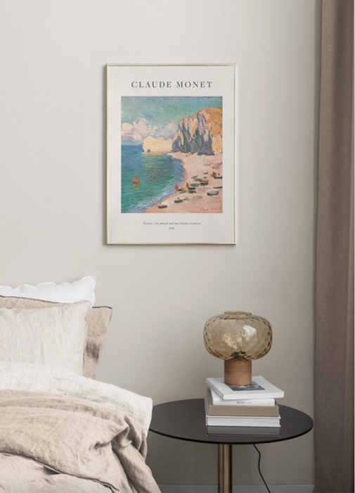 A reproduction of a Monet painting displayed above a nightstand adorned with books and a vintage lamp