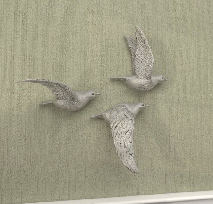 Three silver bird sculptures gracefully displayed on a wall above a neatly made white bed with plush pillows
