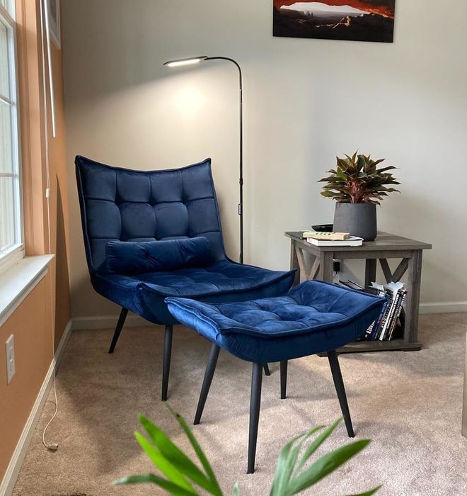A cozy reading nook featuring an adjustable floor lamp, a tufted blue lounge chair, and a wooden side table with a plant sitting atop it