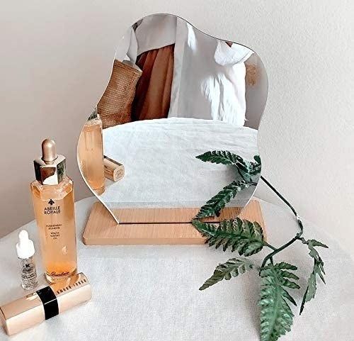 A wavy-shaped mirror resting on a wooden stand