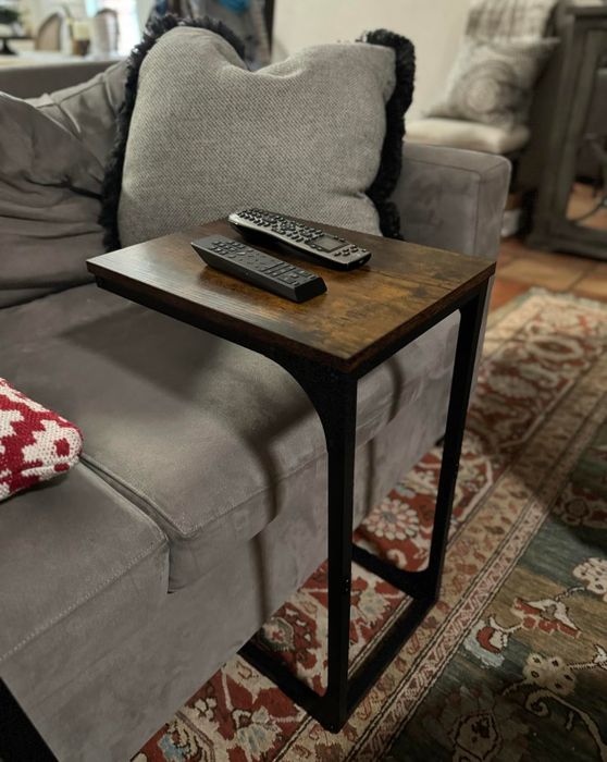 A side table with a wooden top and metal frame placed next to a sofa, holding a remote control