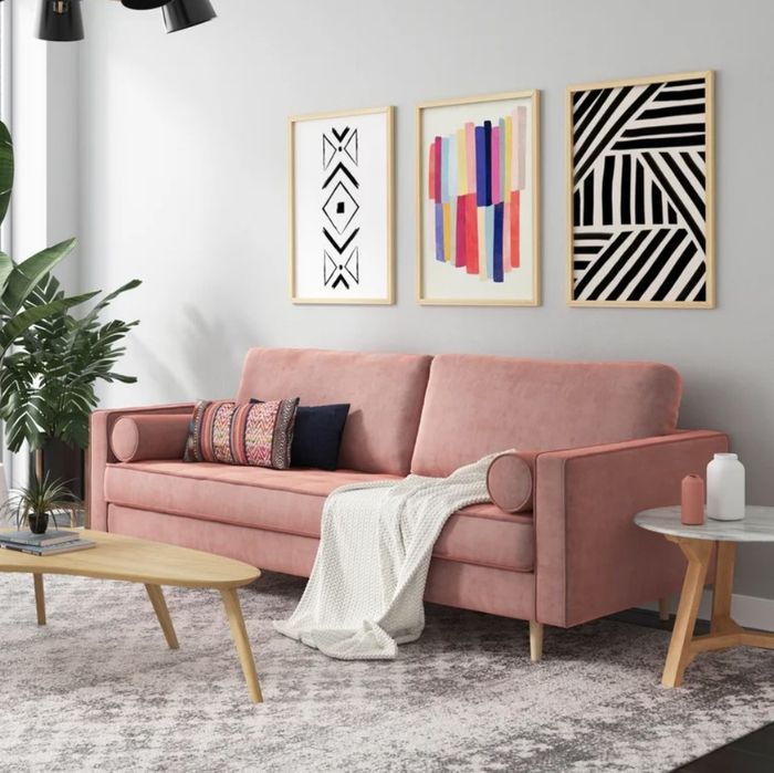 A blush pink velvet sofa in a living room, complete with accent pillows and a throw blanket draped across it for extra comfort