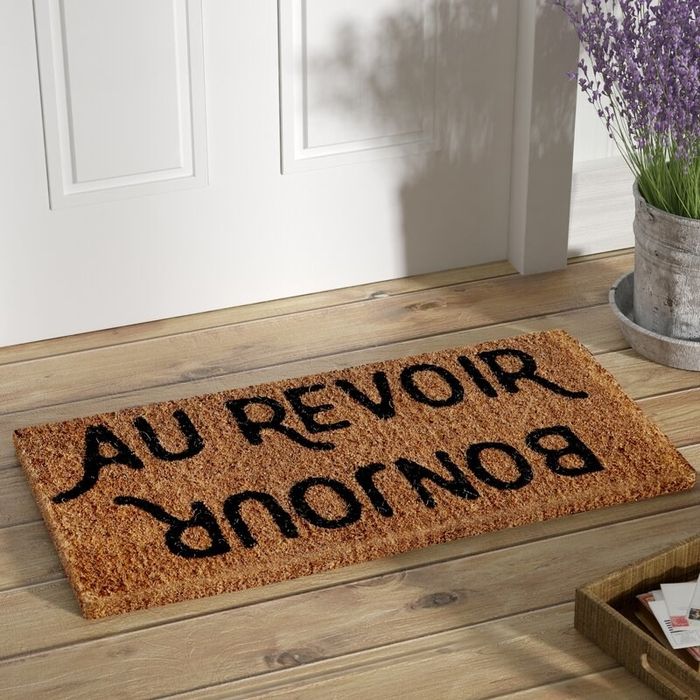 A natural-colored doormat featuring the words 'Bonjour' and 'Au revoir' in black lettering.