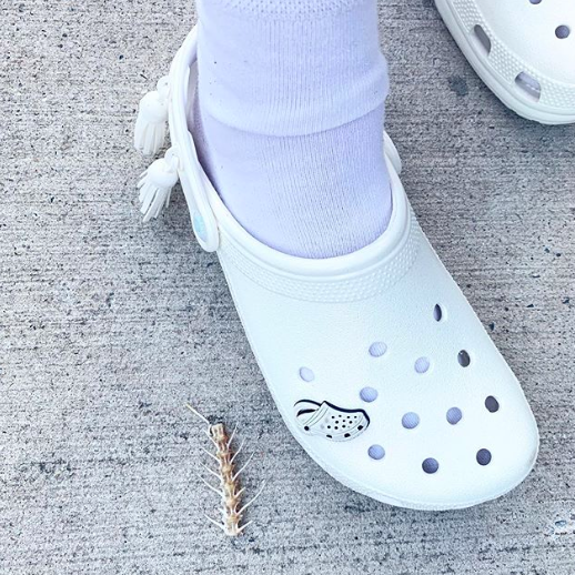 A white pair of Crocs featuring a white Crocs charm inside one of the holes.