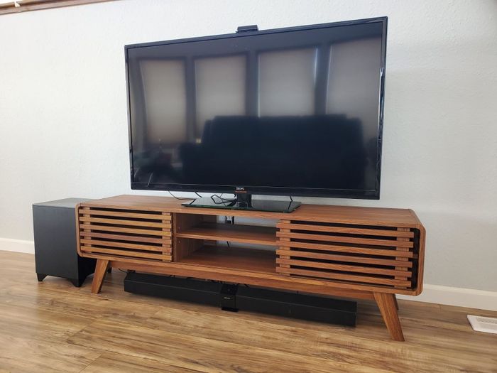 A sleek television resting on a wooden stand, with slatted cabinet doors, set in a modern living room environment
