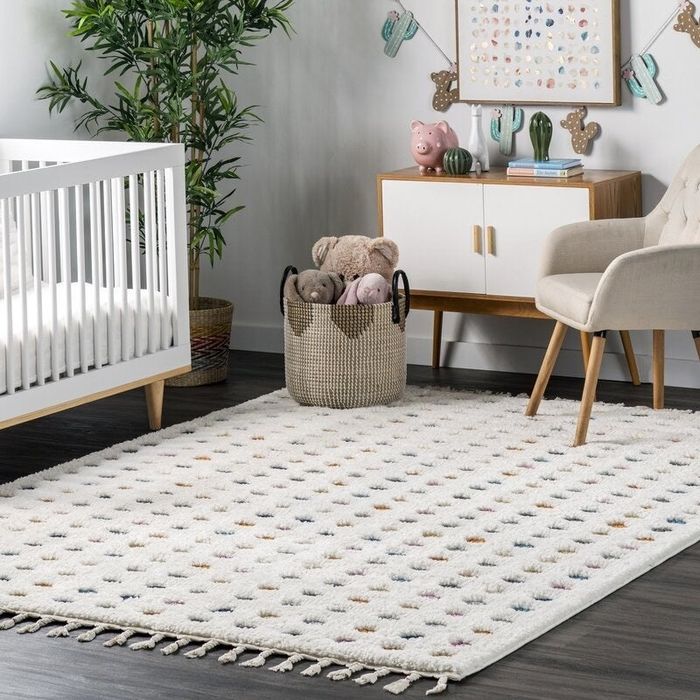 A textured white rug featuring colorful polka dots and tassels, displayed in a well-decorated nursery.