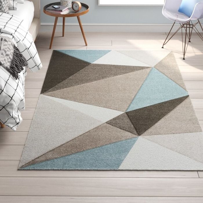 A geometric rug in shades of blue, beige, and brown, laid on hardwood floors in a bedroom.