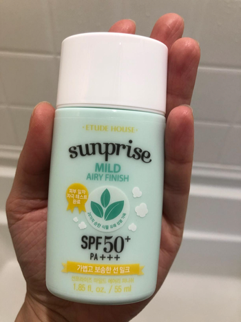 A reviewer holds a green and white bottle of the milk sunscreen, showcasing the product.