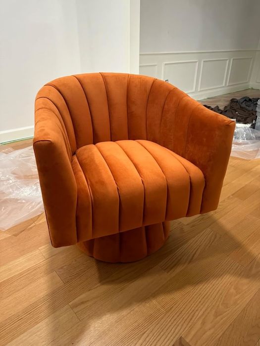 A plush orange chair with a scalloped back and vertical grooves, set on a wooden floor, exuding modern style