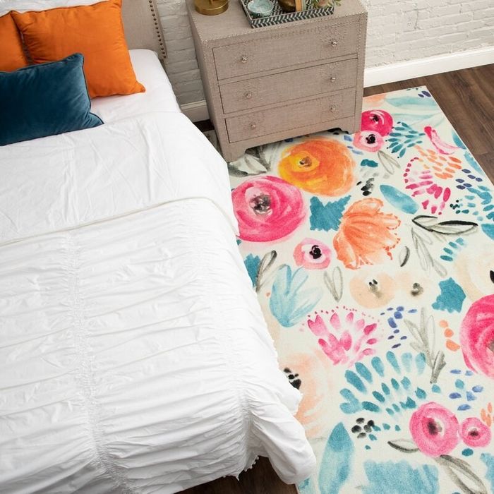 A vibrant floral rug placed next to a bed and nightstand in a cozy bedroom.