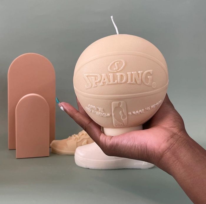 A hand holds a beige candle shaped like a miniature basketball