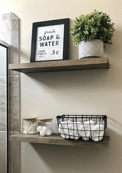 Image of two wooden shelves mounted on a wall, holding baskets and containers filled with toiletries and towels