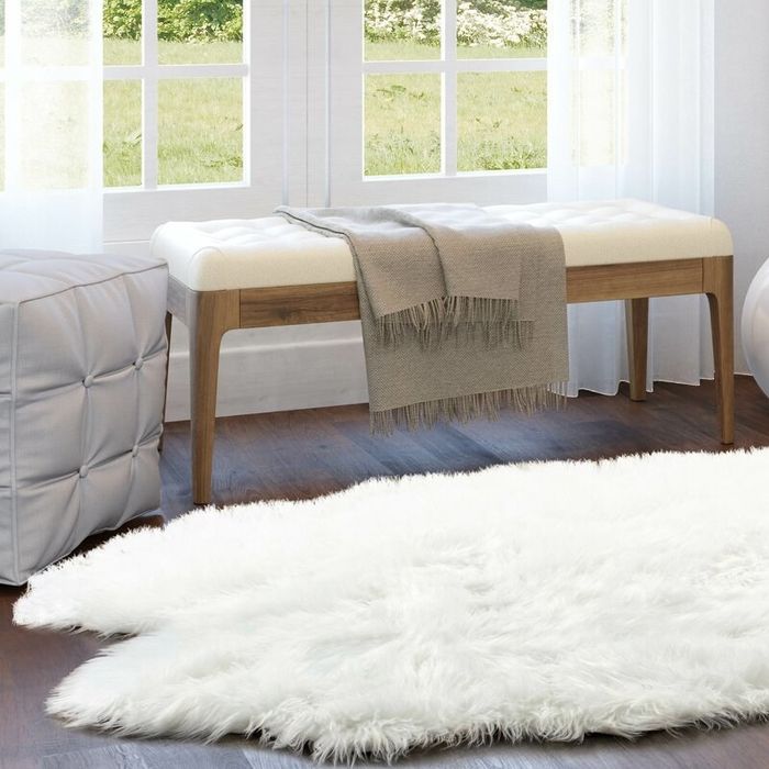 A white faux sheepskin rug positioned next to a bench and pouf.
