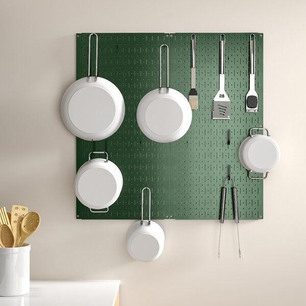 Kitchen tools like pans and spatulas hanging neatly on a green pegboard