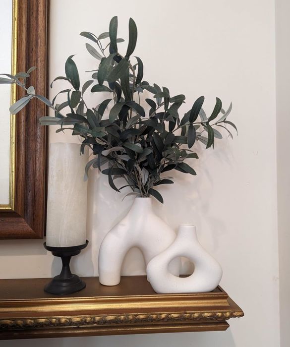 An artificial plant in a white torso-shaped vase, paired with a candle on a shelf. A unique touch of home decor