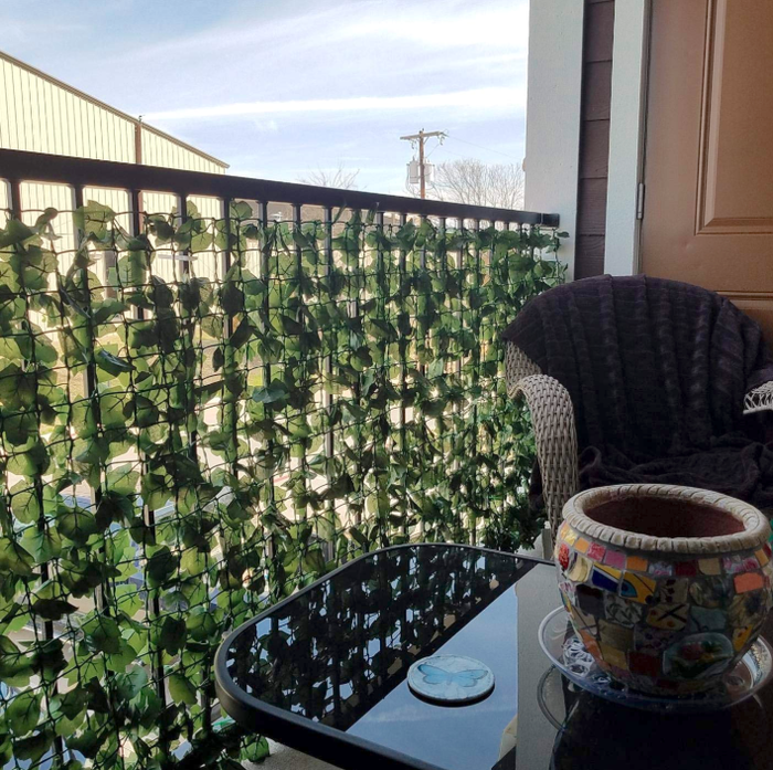 A reviewer's balcony adorned with the ivy; the plastic grid it comes on is rolled up with leaves scattered all over. The coverage is so dense that a car is barely visible on the other side.