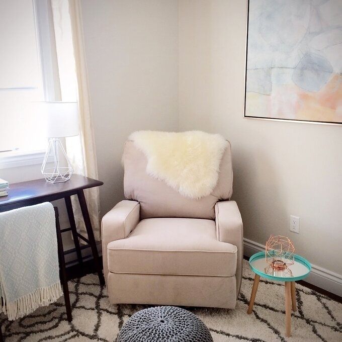 A comfortable chair with a plush throw, a side table with a lamp, and a small accent table