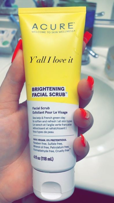 A hand holding a tube of Acure Brightening Facial Scrub with text overlay.