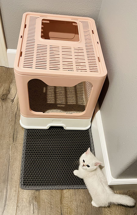 A gray honeycomb-patterned square mat placed next to the cat litter box in the bathroom.