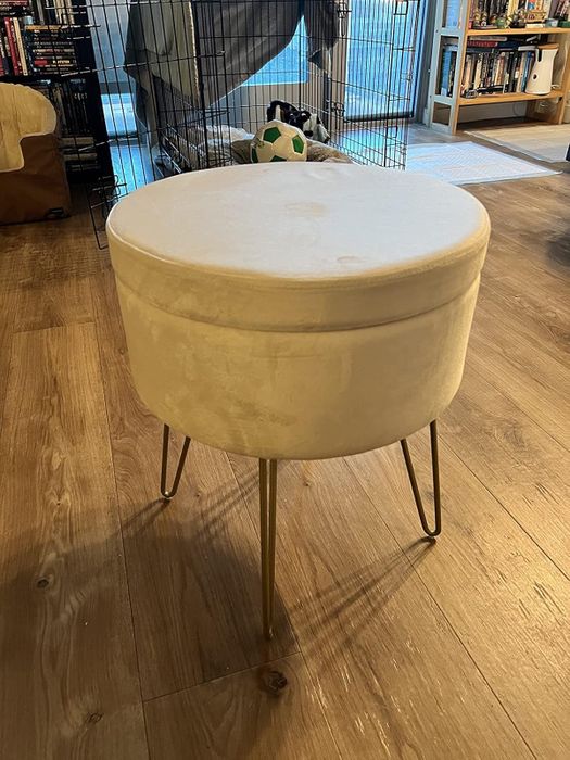A reviewer's round velvet ottoman with sleek metal legs placed in a cozy living room, perfect for modern home interior designs.