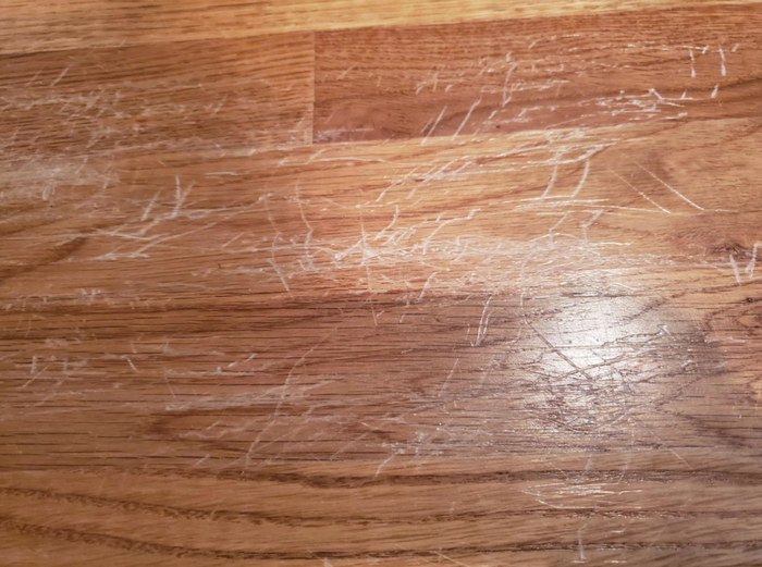 A reviewer's hardwood floor, covered in scratches made by their child jumping on the bed, causing the legs to scrape the surface repeatedly.
