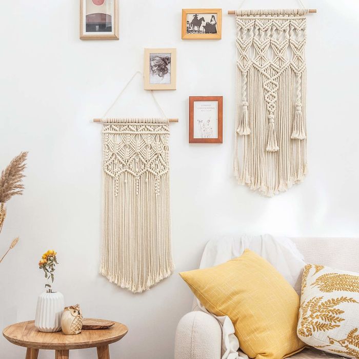 Two distinct macrame pieces hang as part of a gallery wall; one features three tassels cascading down instead of just extra thread.