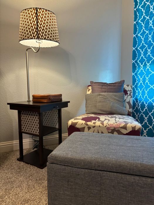 A reviewer’s cozy reading nook, featuring a patterned armchair, a side table, and an attached lamp, creating the perfect spot for relaxation.