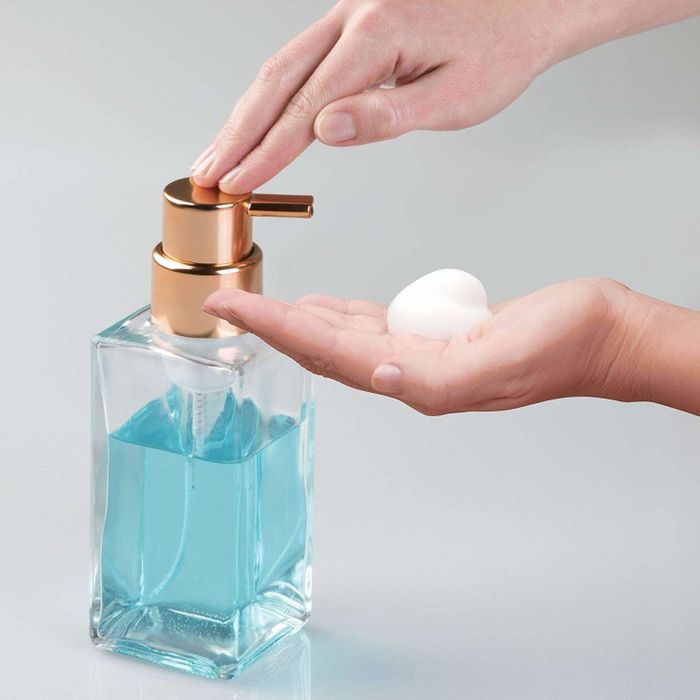 A model dispenses foam from a clear soap dispenser with light blue soap into their hand.