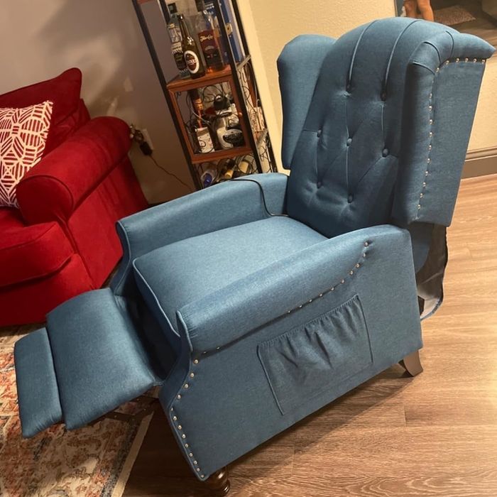 A blue wingback chair with tufted details and nailhead accents, placed in a stylish living room