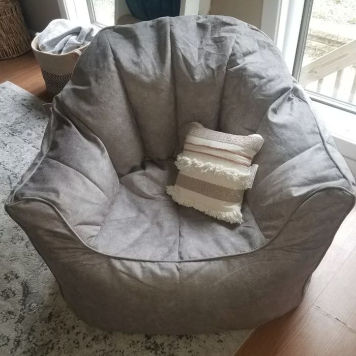A gray bean bag chair with a small decorative pillow, placed next to a window in a cozy room