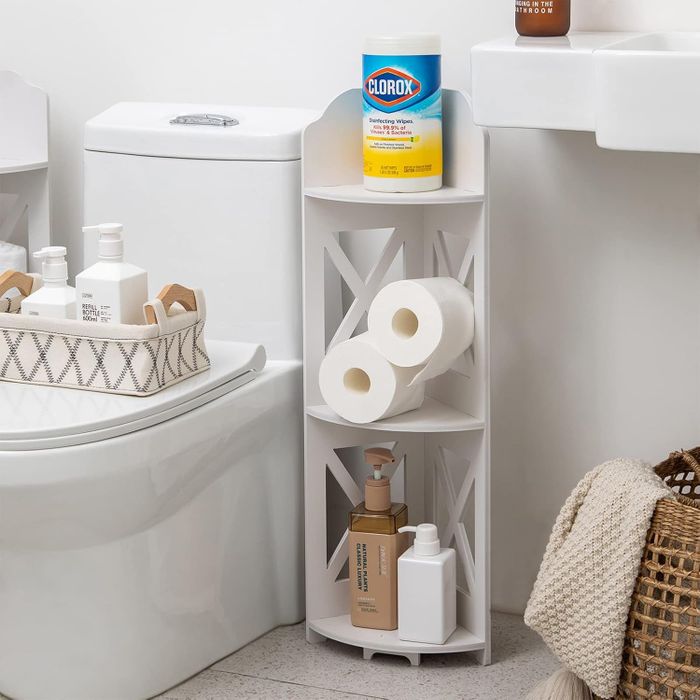 This bathroom corner shelf is organized with cleaning supplies, toilet paper rolls, and toiletries, neatly placed next to a toilet and sink for practical storage.
