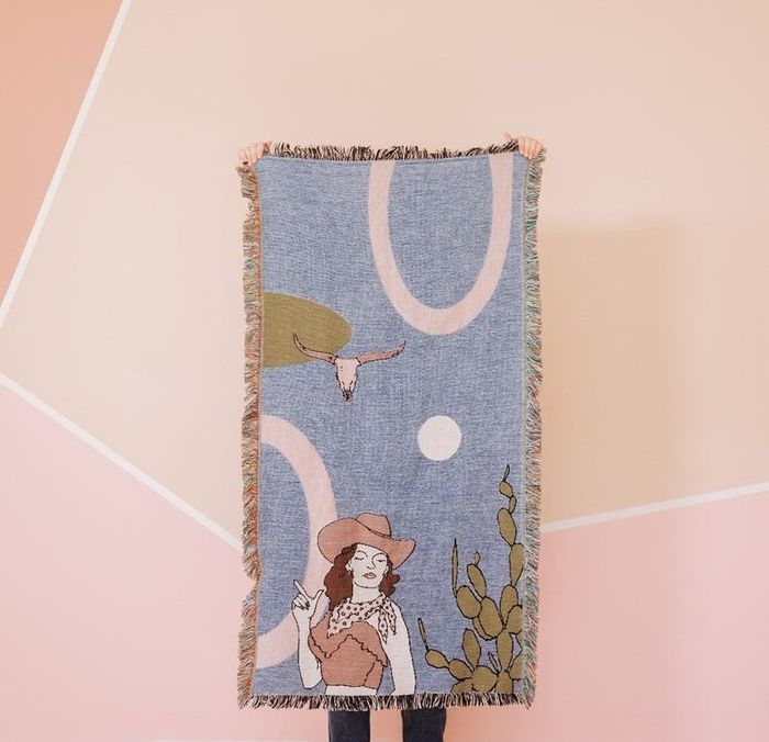 a cozy blanket featuring a cowgirl and cow skull design in soft pastel hues