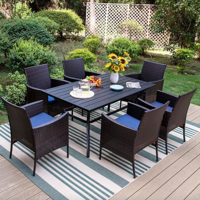 a large black metal dining table with six black chairs featuring blue cushions, set in a beautifully arranged outdoor area