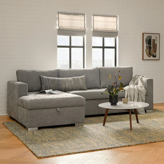 A modern living room features a gray sectional sofa, a coffee table, and a decorative plant, with natural light pouring in through large windows.