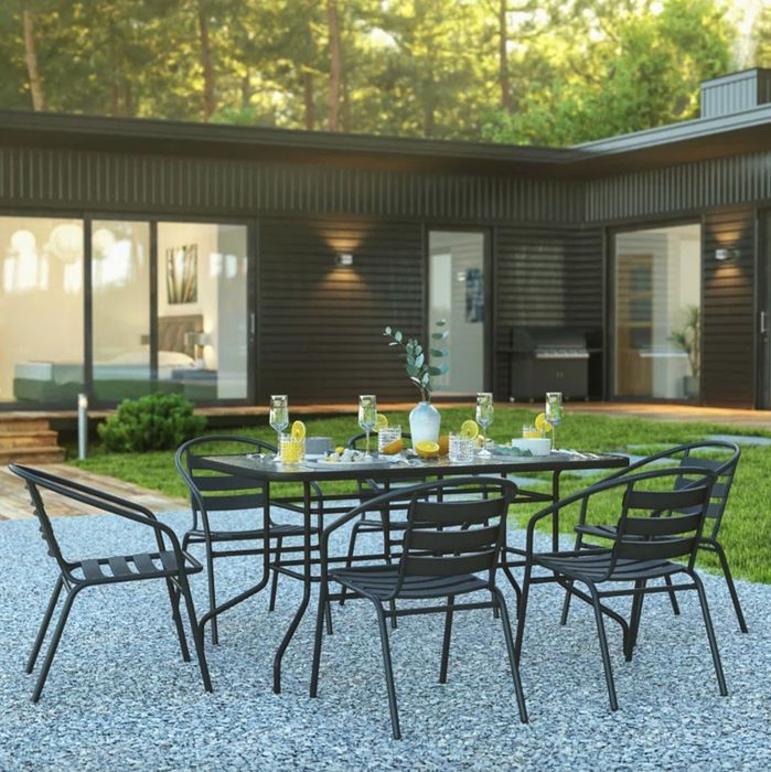 A set of black metal chairs and a glass-topped table placed in a beautifully decorated outdoor space.