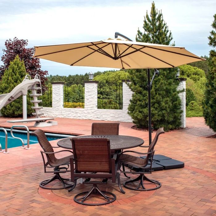 A tan umbrella providing shade over a brown outdoor table on a poolside deck.