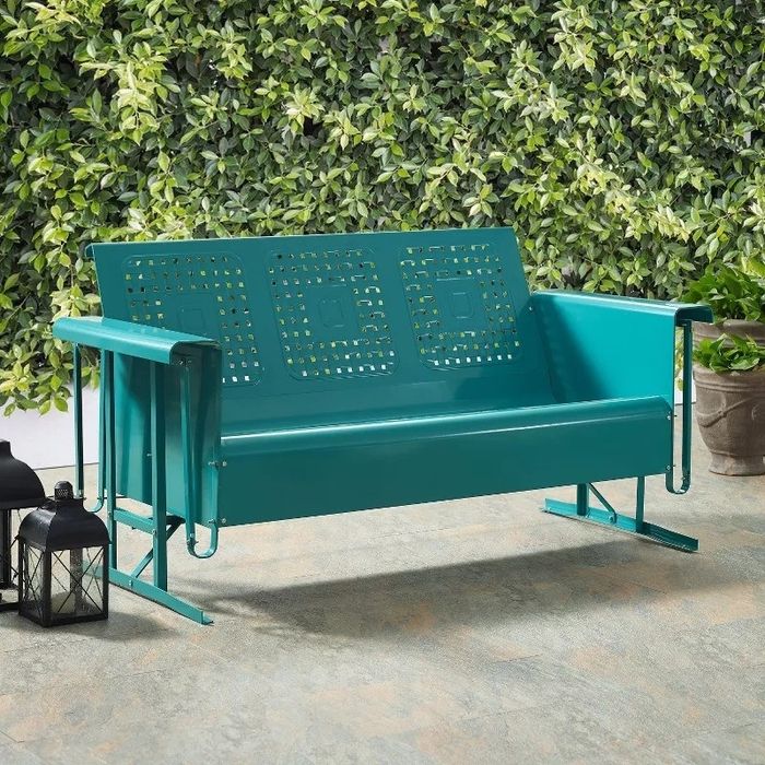 A teal metal outdoor glider bench surrounded by lanterns and greenery, ideal for enhancing your garden or patio decor.
