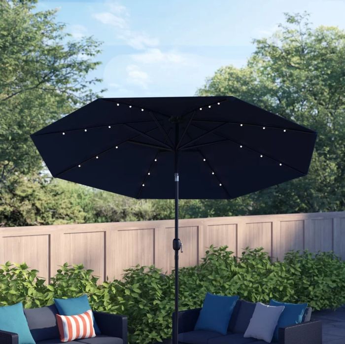 A black umbrella with built-in LEDs on the underside, placed in a beautifully decorated outdoor space.