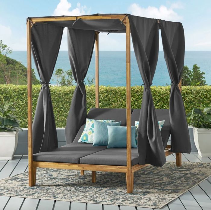A wooden daybed adorned with grey cushions and hanging fabric.