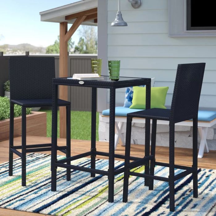 The sleek black tall table and chairs are arranged on a striped rug, completing the look of a chic, decorated outdoor area that invites relaxation and conversation.