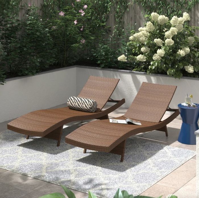 Two dark brown wicker reclining chaises on a patio, each equipped with cushions and blankets for extra comfort.